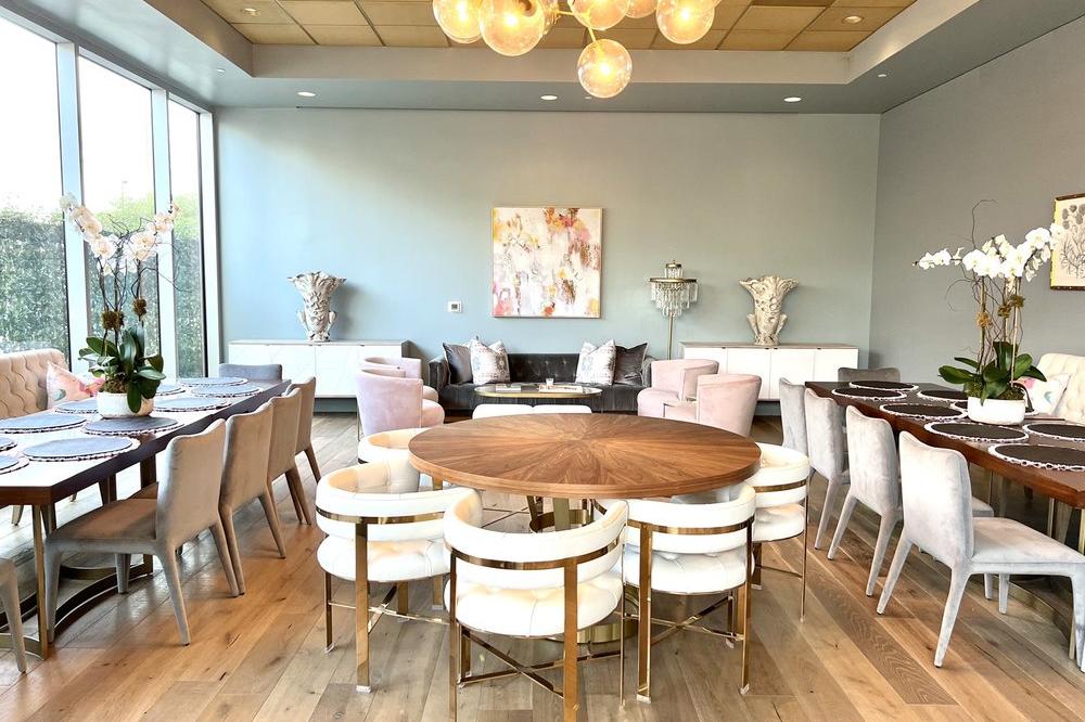 The light-filled event room at Bean & Bottle, with a round wooden table, lounge seating, and floor-to-ceiling windows